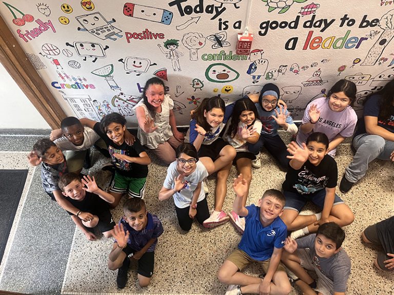 A group of students poses in front of a mural they are creating for the 2024 Summer Discovery Program at Lindbergh Elementary.